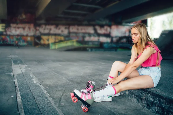 Seriös tjej sitter och drar tillbaka långa skosnören på rätt rullskidor. Flickan är koncentrerad till denna åtgärd. Hon kommer att vara redo för inlines. — Stockfoto