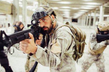 Cesur ve ciddi asker ile onun combads parlak uzun odada duruyor. Diğer iki savaşçı için farklı açılardan arıyoruz iken sakallı adam nişan alıyor. Olarak çalıştıkları bir