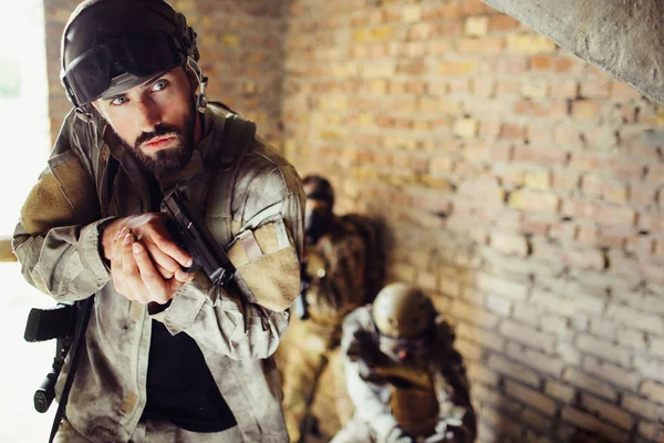 Careful soldier is standing with his combads in a room. He is holding a gun. Guy is looking straight. He behaves very careful. — Stock Photo, Image