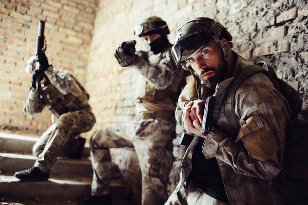 Три воина стоят на лестнице и позируют. Человек спереди смотрит прямо вперед и держит пистолет. Второй парень целится прямо вперед. Третий смотрит вверх с винтовкой
.