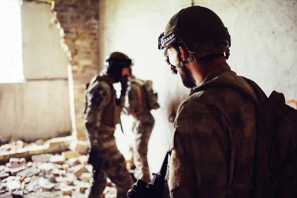 A ppicture of soldiers standing in a rooom near ruined wall. Two of them are standing towards each other while thrid one is looking at them. They are having some rest. — Stock Photo, Image