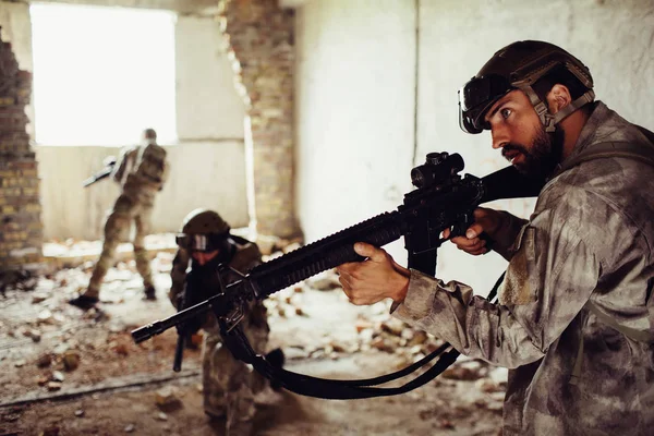 A picture of thhree warriors standing in different positions in one ruined room. Bearded guy holds rifle, the second one is standing in the middle of room while the third one is standing closer to