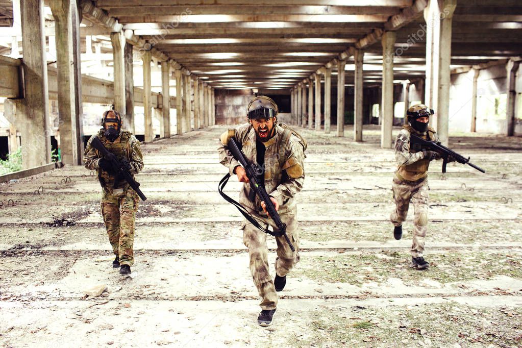 Three warriors with equipment is running down big and bright room. Two of them are looking to the sides while the man in front is looking straight and screaming. All of them have rifles in hands.