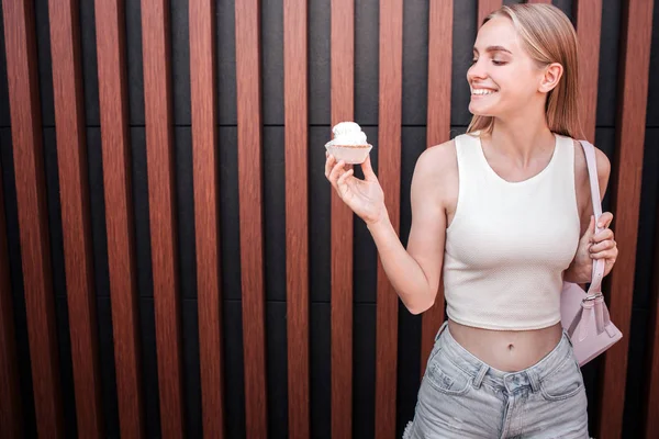 Hay un sabroso y delicioso panqueque que la chica está sosteniendo en la mano. Ella lo mira y sonríe. La chica es delgada y bien construida. Aislado sobre fondo rayado . —  Fotos de Stock