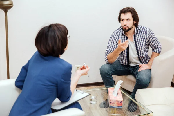 Mann und sein Arzt unterhalten sich. Es ist sehr emotional. Der bärtige Typ winkt mit der Hand. Der Therapeut tut dasselbe. sie sitzen im weißen Raum. — Stockfoto