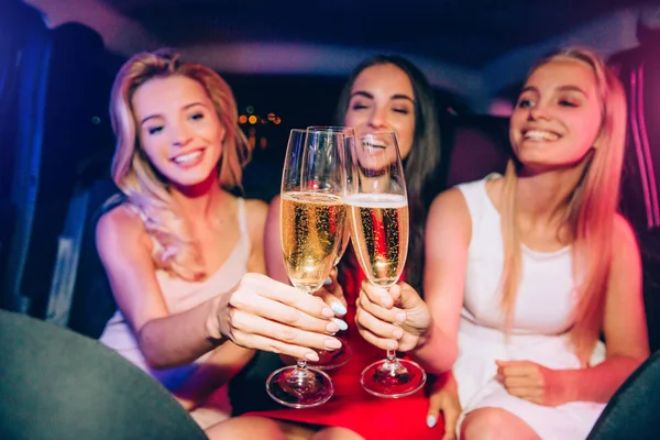 Ein Bild von Mädchen, die im Auto sitzen und eine Brille klirren. Sie blicken auf Gläser voller Champagner und lächeln. Mädchen haben Spaß. — Stockfoto