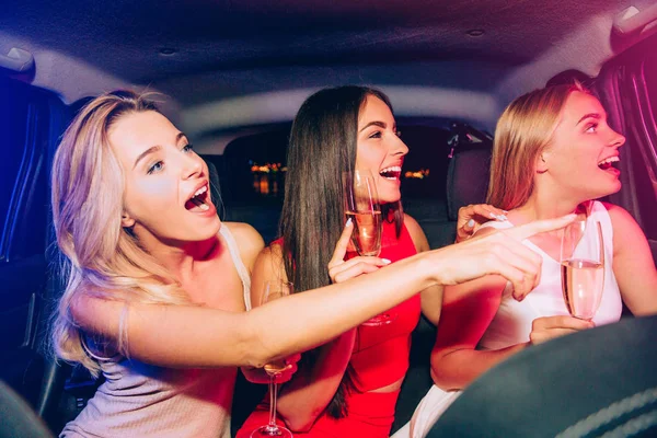 Aufgeregte Mädchen sitzen im Auto und schauen nach rechts. Die jungen Frauen lachen. Blondes Mädchen zeigt nach rechts. Alle sind erstaunt. — Stockfoto