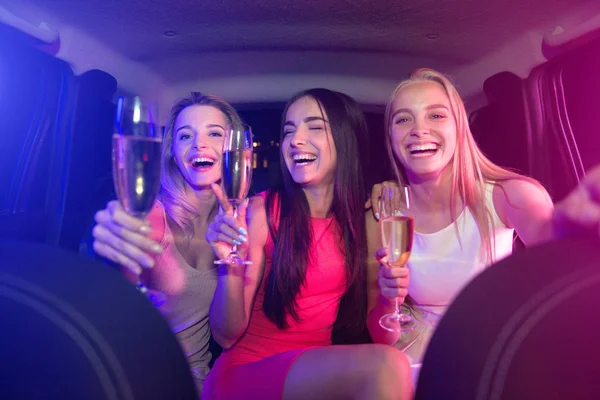 Happy and delightful girls are sitting in car and holding glasses of champagne in hands. They are laughing and smiling. Some of them are looking on camera. They have a party. — Stock Photo, Image