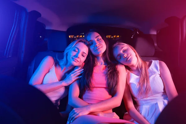 Lugn och fridfull flicka sover i bilen. Brunett flicka sitter mellan två blonda sådana. De är tupplur på brunetter axlar. Dess kväll utanför. — Stockfoto