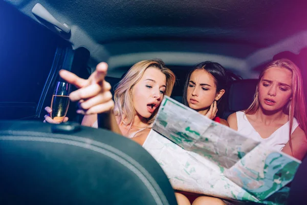 Drei Mädchen sitzen im Auto und schauen auf die Landkarte. Blondes Mädchen zeigt nach vorne. Sie reden miteinander. Ein anderes blondes Mädchen ist aufgebracht. Brünette sieht sehr ernst aus. — Stockfoto