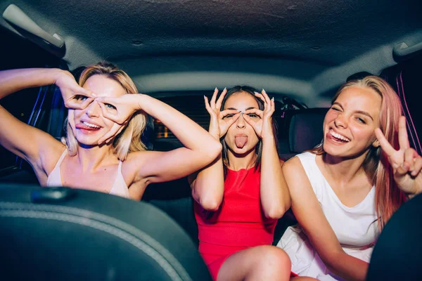 A picture of funny girls making funny figures aroung their eyes. They are showing uo their tongues. One of them is showing piece symbol with her fingers.