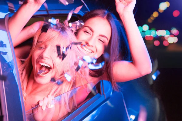 Ausdrucksstarke Mädchen schauen aus dem Autofenster und amüsieren sich. Brünettes Mädchen winkt mit der Hand nach draußen. sie sind aufgeregt und glücklich. — Stockfoto