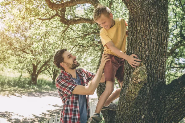 Father and son are playing with each other. Guy is supporting his child. Boy is looking down at father. They are smiling. Both of them are happy. — Stock Photo, Image