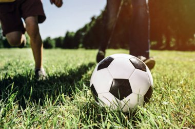 Bacaklar iki kişinin futbol oyunu oynarken bir resim. Sulu ve yeşil çimenlerin üzerinde oynuyorlar. Dışarıda hava güneşli.