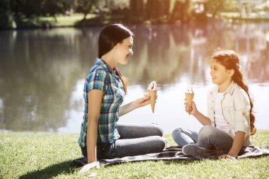 Güzel anne ve kızı yüz yüze yakın küçük bir göl Park'ta oturuyor. Her biri con dondurma holding ve birbirine bakarak. Onlar gülüyor.