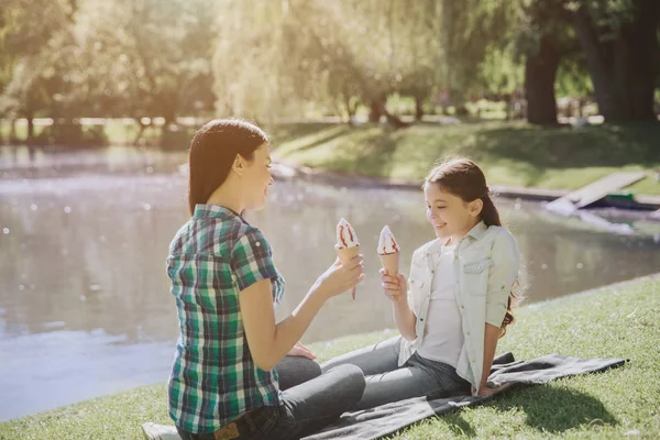 Una foto de mamá y su hija sentadas en una manta cerca del lago. Están sosteniendo helados en las manos. La chica está mirando el helado. La mujer está mirando al niño. . — Foto de Stock