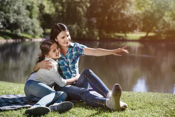 Une famille heureuse est assise ensemble. Femme étreint sa fille d'une main et pointant droit vers l'avant. La fille se penche sur la mère et regarde dans la même direction . — Photo