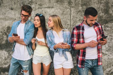 Dört genç ve meşgul insanlar birlikte gri arka plan üzerinde duran ve onların telefon arıyor. Onlar ciddi amd konsantre vardır. Yalnızca sağdaki adam biraz gülümsüyor.
