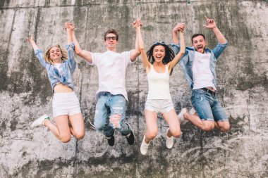 Harika ve güzel insanlar havada atlama vardır. Onlar ellerini havada çok tutuyor. Gri arka plan üzerinde bir şirkettir. Bunlar pozitif ve mutlu.