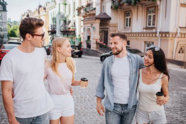 İki çiftler birlikte sokakta yürürken. İlk çift ikinci arıyor. Kızlar kahve elinde tutuyor. Memnun ve neşeli görünüyorlar.