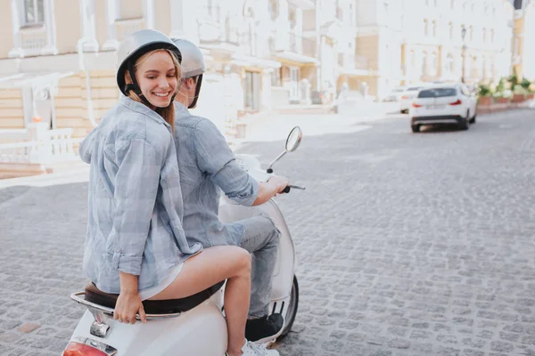 Ελκυστική κοπέλα ποζάρει στην κάμερα. Ψάχνει πίσω. Το κορίτσι και ο φίλος της φορούν κράνη. Αυτός οδήγηση της μοτοσικλέτας. — Φωτογραφία Αρχείου