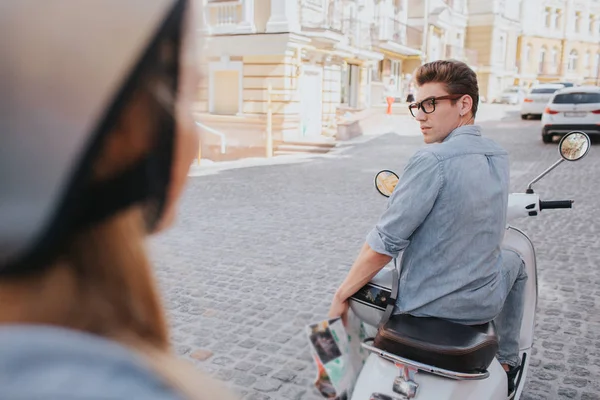 Attraktiver Kerl sitzt auf Motorrad und schaut Mädchen an. Er ist gutaussehend und selbstbewusst. Mädchen schaut ihn an. sie trägt Helm. — Stockfoto
