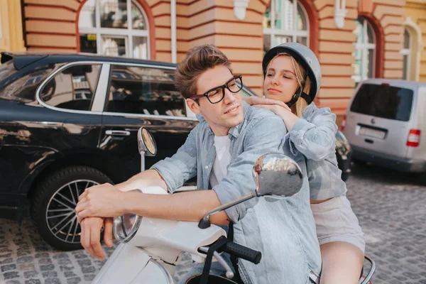 Tired girl is sitting behind her boyfriend on motorcycle and leaning to him. She is looking at him. Guy is leaning to control handles and looking to the right. He looks confident. — Stock Photo, Image
