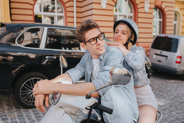 Tired girl is sitting behind her boyfriend on motorcycle and leaning to him. She is looking at him. Guy is leaning to control handles and looking to the right. He looks confident.