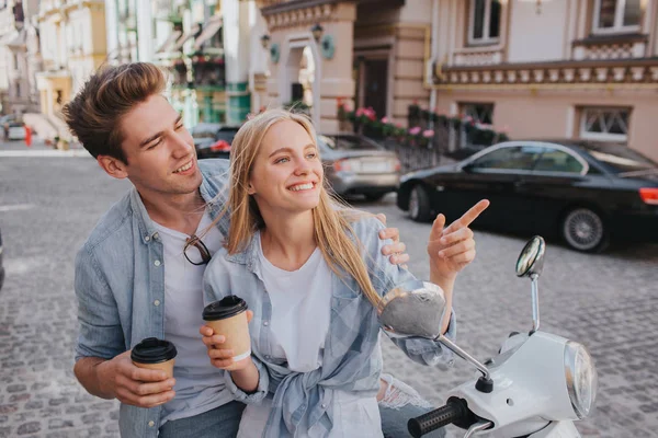 Beautiful couple is sitting together on motorcycle anf looking at each other. They are holding cups of coffee in hands. They are having some rest and fun. — Stock Photo, Image