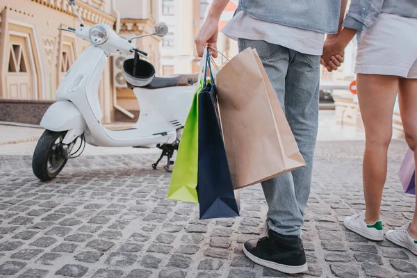 Happy girl is holding shopping bags in hand and enjoying. She is looking up and smiling. Guy is driving motorcycle. He is looking at her and smiling. — Stock Photo, Image