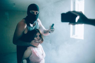 Başka bir resmi kaçıran ve onun kurbanı. Adam maske takıyor. O kızın arkasında duran ve silah tutan. Kamerada arıyorlar. Başka bir adam video kaydediyor. Kız ile ipler bağlıdır.