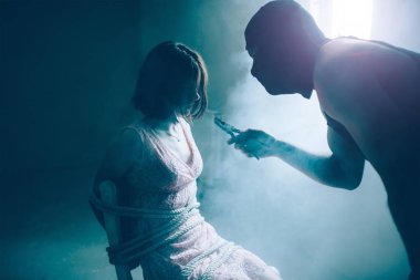 Maskeli adam onun kurbanı yakın duran ve ona bakıyorsun. Pense elinde tutuyor. Kız sandalyeye bağlanmış oturuyor. O yorgun ve bitkin.