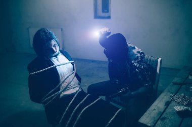 Sandalyeye sittig yaşında. Cesedini bağlıdır. O katiller alnına küçük ampul gelen ışık nedeniyle onun kaçıran bakamıyorum. Maskeli adam onun kurbanı önünde oturuyor.