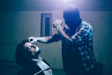 Genç adam sandalyeye bağlanmış ve gözleri kapalı tutarak oturuyor. Stqanding onu ve onun elinde olan kamera video kayıt önünde katildir. Adam kaçıran kurbanının alnına dokunuyor.