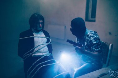 Siyah maskeli ciddi adam el üstünde tutma tabanca olduğunu ve bir tane de ışıklar. Onun kurbanı arıyor. İş adamı sandalyeye oturuyor. Kapalı ağızla oturan ipleri amd ile bağlı.