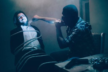 Bir resim video kötü katil kayıt. O elinde bıçakla kurban thoat yakın ve buna bakıyor. İş adamı sandalyeye bağlanmış oturuyor. O korkuyor. Adam keskin bıçak önlemek çalışıyor.