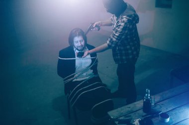 Adam kaçıran kurbanını duran ve elinde silah başını yakın. İş adamı sandalyeye oturuyor. Halatlarla bağlanmış. Çaresiz ve korkuyor ve dehşete adam.