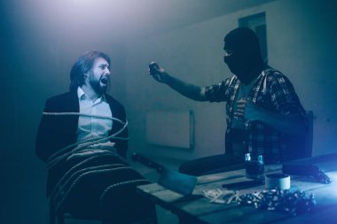 Adam çığlık ve kameraya bakıyor. O korkuyor. Adam ile ipler bağlanır. O korkuyor. Adam kaçıran sittting ve video kaydı var. Ayrıca o bıçak ve alkol, tablo üzerinde zincirleri vardır.