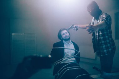 Suite adam acı çekiyor. O ile oturuyor onun sandalyeye bağlı iyiye işaret. Adamın gözleri kapalı tutuyor. Maskeli adam kurban kafa yakın silah tutan ve kamera işaret. Video kaydı.