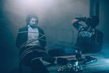 Suite kızgın adam sandalyeye bağlanmış oturuyor. Çocuk hırsızı bakıyor. Maskeli adam onun kurbanı oturan ve alkol şişeden içme. Zincirler, bıçak ve tablo kasette.