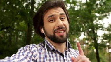 Adam o kamerayı ve bakmak belgili tanımlık video kayıt video kapatın. O kamera için konuşma ve el sallayarak. Adam parkta yürüyor. O neşeli ve çekici..