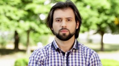 Ciddi adam parkta duran ve doğruca kameraya bakıyor. O ciddi ve konsantre. O biraz el sallayarak ve gözleri yanıp sönüyor. Bir parça saç rüzgar esiyor.