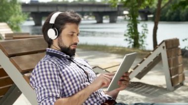 Adam bankta yalan ve kulaklık üzerinden müzik. Ayrıca o tablet holding ve ekranda yazmaya. Adam ekrana bakarak ve onun pompalara hareket. Aşağı ve yukarı doğru kayıyor. Adam gülümsüyor.