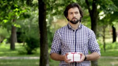 Adam parkta duran ve bir hediye tutarak. O sallıyor. Adam sol ve sağ ve onun saatler için yandan görünüyor. O zaman şu anda farklı kenarlara ve seyretmek o görünüyor sonra adam arıyor