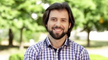Olumlu ve sakallı bir adam kameraya bakıyor ve biraz gülümseyen. Sonra gülmeye başladı. Kamerada beyaz dişlerini gösterir. Adam kafa ile birkaç kez sallayarak.