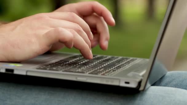 Die Finger tippen Wörter auf die Tastatur des Laptops. Er hält Computer auf den Beinen. Mann sitzt draußen im Park. Er tippt sehr schnell. — Stockvideo