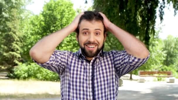 Um homem espantado está a olhar para a câmara. Ele está sorrindo alegre. O tipo toca no cabelo e agarra-o com as mãos. Então ele está acenando com as mãos e tocando a cabeça. Cara olha para baixo, toca barba e solta em linha reta . — Vídeo de Stock