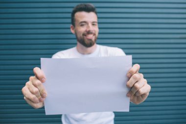 Güzel ve yakışıklı bir adam kameraya bakıyor. İki eliyle kağıda boş tutuyor. Bu kameraya gösteren 's. Çizgili ve mavi arka plan izole.