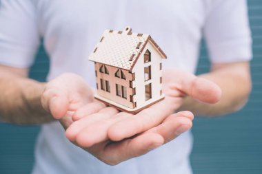 Ayakta ve tutmak ahşaptan yapılmış bir ev oyuncak adam resmi. Açık renk vardır. Adam iki elinle tutuyor. Çok doğru. Çizgili ve mavi arka plan izole.