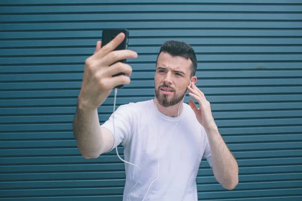 A picture of concentrated man looking at phone he has in hands. Guy is listening to music and posing. He is taking selfie. He looks cool. Isolated on striped and blue background. — Stock Photo, Image